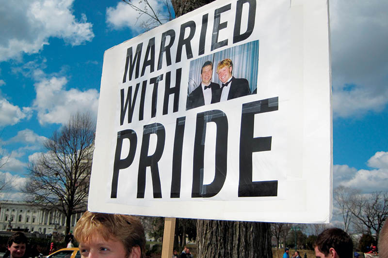 Um homem segura um cartaz onde está escrito "casamos com orgulho".